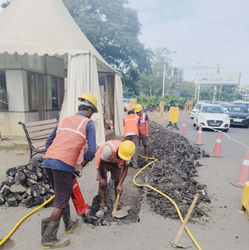 Field team breaking ground for duct trenching near a city flyover
