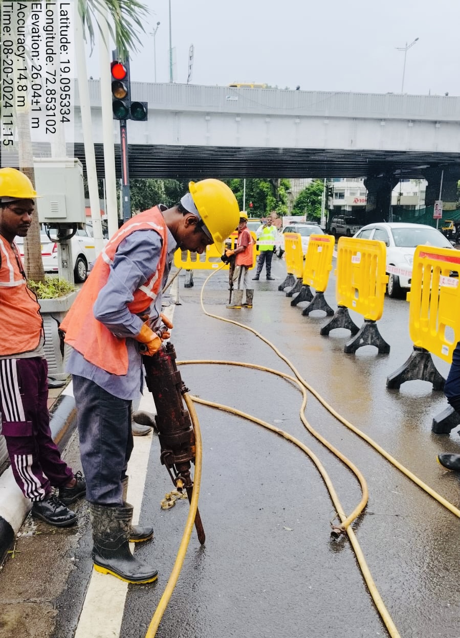 Jackhammer road-cutting operation beneath a flyover for duct laying