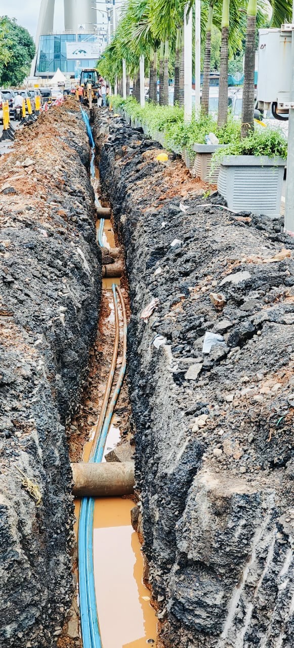 Open trench with HDPE ducts laid along a palm-lined road