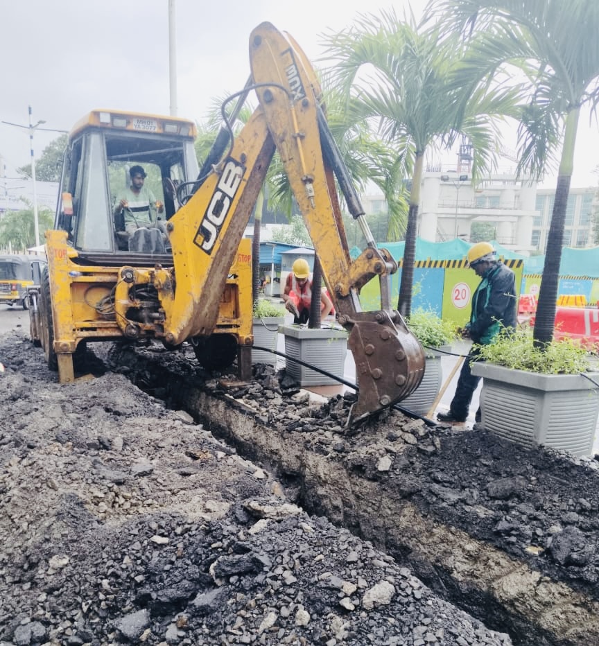 Backhoe digging a duct trench near a modern glass building